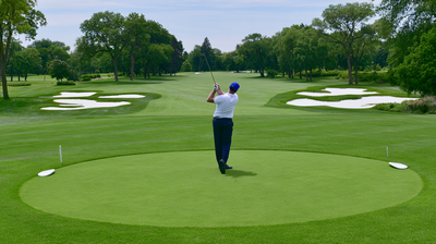 A golfer mid-swing on a tee surrounded by trees